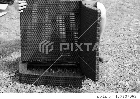 Person assembling dark woven patio furniture outdoors. Sections are being connected. Person assembling dark woven patio furniture outdoors. Sections are being connected. 137807965