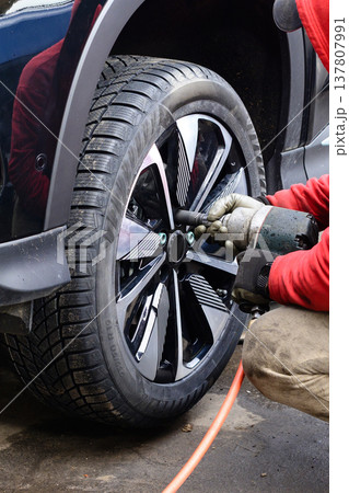 Worker changes tire on a black vehicle at a garage during daylight hours using a power tool 137807991