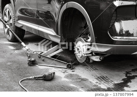 Car repair takes place at an auto shop with a jack lifting a vehicle for tire maintenance and inspection in the afternoon 137807994
