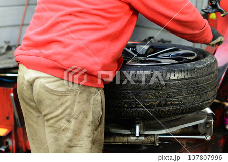 Worker changes tire in a garage during the day, focused on removing the old tire from the wheel rim 137807996