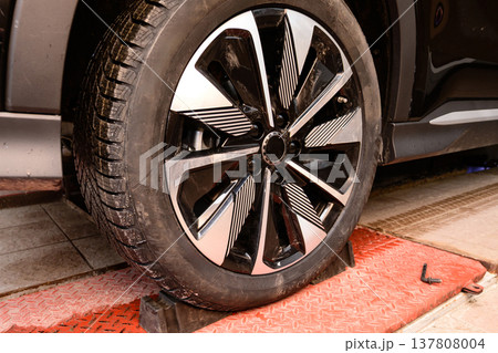 Wheel alignment and alignment on the car service platform. Car tire being repaired while on service lift in a workshop during daytime in the city center Wheel alignment and alignment on the car service platform. Car tire being repaired while on service lift in a workshop during daytime in the city center 137808004
