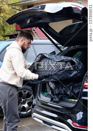 Man loading a tire into the trunk of a car at a location on a rainy day in an urban area Man loading a tire into the trunk of a car at a location on a rainy day in an urban area 137808031