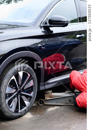 Mechanic works on a black SUV using a jack to lift the vehicle in a garage 137808035