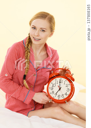 Sleepy woman wearing pajamas holding clock 137808165