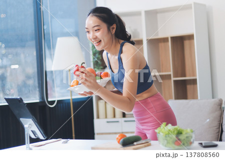 Fit young Asian women in activewear sitting on yoga mat and eating fresh vegetable salad after workout, representing clean eating, fitness lifestyle, wellness routine and health balance. 137808560