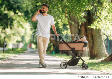 Talking by phone. Father is with cradle, having a walk in the park Talking by phone. Father is with cradle, having a walk in the park 137808644