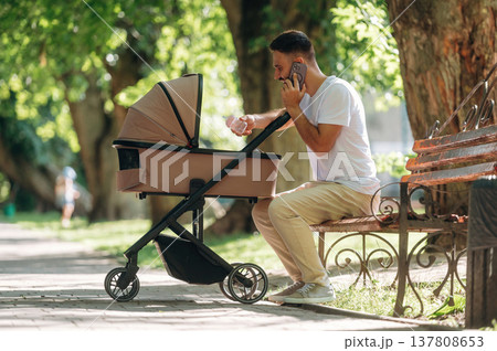 Talking by phone. Father is with cradle, having a walk in the park 137808653