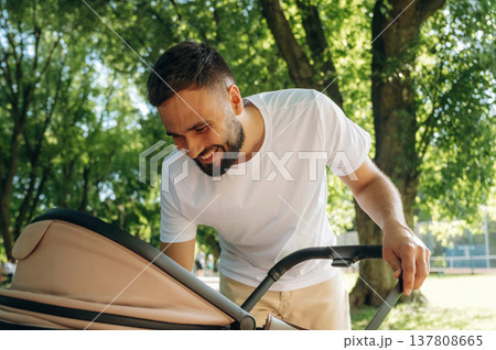 Taking care of baby, looking into a cradle. Father is having a walk in the park 137808665