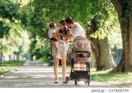 Family conception. Couple is with daughter and cradle are having a walk Family conception. Couple is with daughter and cradle are having a walk 137808754