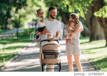 Little baby in hands. Couple is with daughter, newborn baby and cradle are having a walk Little baby in hands. Couple is with daughter, newborn baby and cradle are having a walk 137808927
