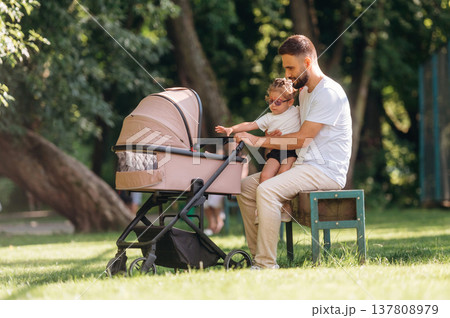 Man with his daughter and cradle in the park Man with his daughter and cradle in the park 137808979