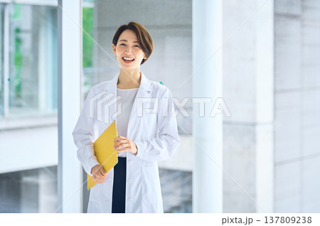 病院やクリニックのロビーでバインダーを持ち笑顔で立つ白衣の日本人女性(医師・薬剤師・研究者) 病院やクリニックのロビーでバインダーを持ち笑顔で立つ白衣の日本人女性(医師・薬剤師・研究者) 137809238