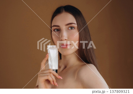 Brand new cream, quality product. Young woman is against background Brand new cream, quality product. Young woman is against background 137809321