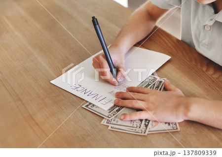Close-up hands writing finance notes on paper with dollar bills on wooden desk, personal budget planning and money management concept, indoor lifestyle overhead shot 137809339