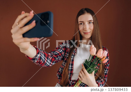 Doing selfie, holding flowers. Woman in casual clothes is against background 137809433