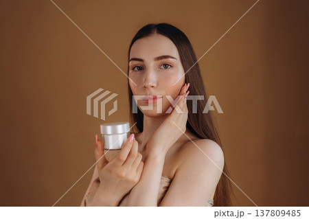 Advertisement for the facial cream. Young woman is against background 137809485