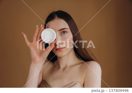 White cream for the face. Young woman is against background 137809496