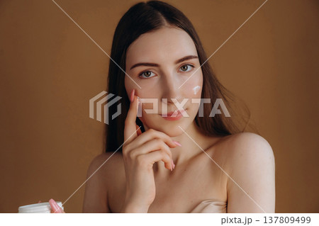 Beauty conception, facial cream. Young woman is against background Beauty conception, facial cream. Young woman is against background 137809499