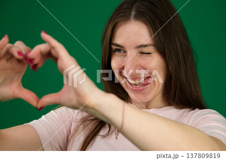 Various emotions of a European woman in a pink T-shirt and black pants on a green background with long brown hair in different poses Various emotions of a European woman in a pink T-shirt and black pants on a green background with long brown hair in different poses 137809819
