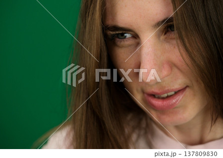 Various emotions of a European woman in a pink T-shirt and black pants on a green background with long brown hair in different poses 137809830