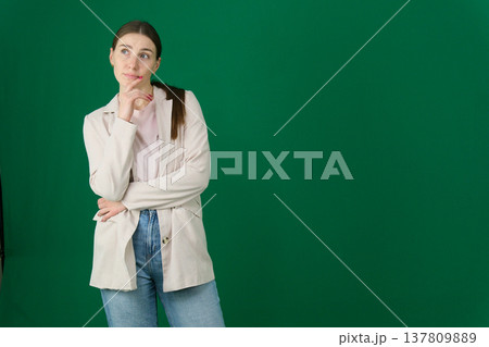Various emotions and poses of a woman in a beige jacket and jeans, wearing a pink European T-shirt with her hair pulled back into a ponytail, against a green background 137809889