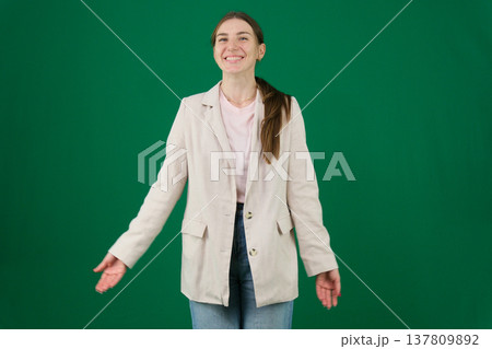 Various emotions and poses of a woman in a beige jacket and jeans, wearing a pink European T-shirt with her hair pulled back into a ponytail, against a green background 137809892