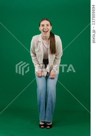 Various emotions and poses of a woman in a beige jacket and jeans, wearing a pink European T-shirt with her hair pulled back into a ponytail, against a green background Various emotions and poses of a woman in a beige jacket and jeans, wearing a pink European T-shirt with her hair pulled back into a ponytail, against a green background 137809894