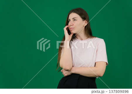 Various emotions of a European woman in a pink T-shirt and black pants on a green background with long brown hair in different poses 137809896