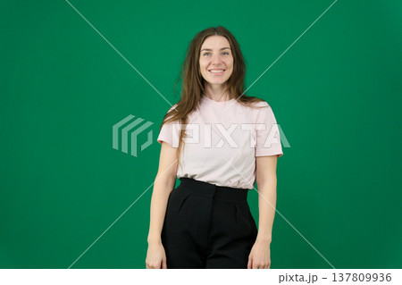 Various emotions of a European woman in a pink T-shirt and black pants on a green background with long brown hair in different poses 137809936