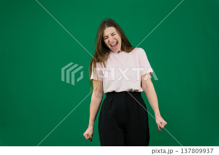 Various emotions of a European woman in a pink T-shirt and black pants on a green background with long brown hair in different poses Various emotions of a European woman in a pink T-shirt and black pants on a green background with long brown hair in different poses 137809937