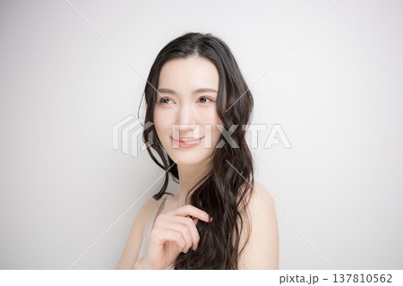 白背景に綺麗な黒髪をなびかせるロングヘアでパーマの女性　ヘアケアやトリートメントイメージ 137810562