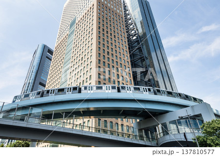 Low-angle view of a New Transit Yurikamome line train running on the elevated track with modern skyscrapers in Shiodome, Minato, Tokyo, Japan. It's an automated guideway transit service in Tokyo. Low-angle view of a New Transit Yurikamome line train running on the elevated track with modern skyscrapers in Shiodome, Minato, Tokyo, Japan. It's an automated guideway transit service in Tokyo. 137810577