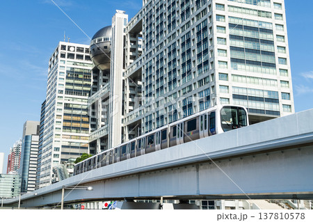 View of a New Transit Yurikamome line train running on the elevated track, driving past the Fuji Television building in Koto, Tokyo, Japan. It's an automated guideway transit service in Tokyo. 137810578
