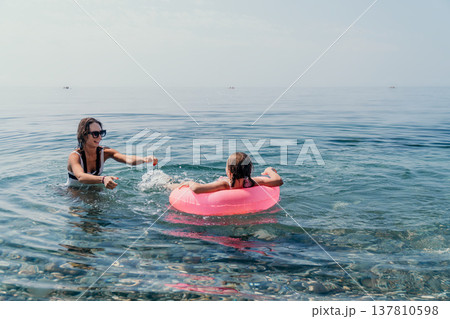 Mother daughter swimming together in the clear blue sea with a pink inflatable ring during a summer family vacation Mother daughter swimming together in the clear blue sea with a pink inflatable ring during a summer family vacation 137810598