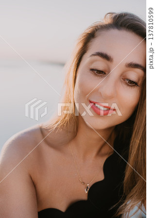 Woman portrait sunset Beautiful young female looking down with a gentle smile during golden hour at the beach for travel and lifestyle Woman portrait sunset Beautiful young female looking down with a gentle smile during golden hour at the beach for travel and lifestyle 137810599