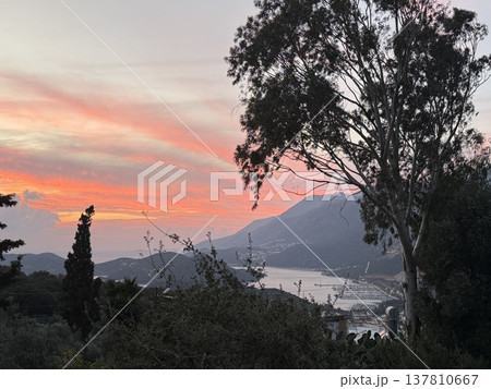 Sunset over coastal landscape with colorful sky and distant mountains, viewed through trees Sunset over coastal landscape with colorful sky and distant mountains, viewed through trees 137810667