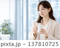 オフィスの窓辺でコーヒーを持つ女性会社員のライフスタイル 137810725