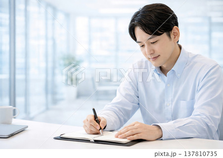 オフィスデスクで手帳に予定を書き込む男性会社員 137810735