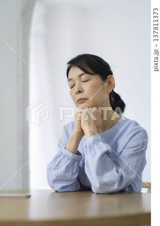 両手に顎を乗せて目を閉じる50代後半の女性 137811373