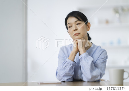 両手に顎を乗せて物思いにふける50代後半の女性 137811374