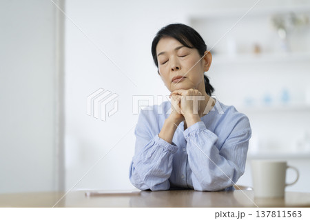 両手に顎を乗せて目を閉じる50代後半の女性 137811563