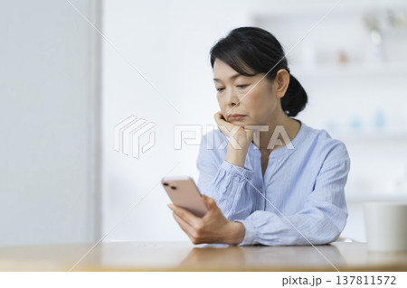 スマートフォンを見ながら考え込む50代後半の女性 スマートフォンを見ながら考え込む50代後半の女性 137811572