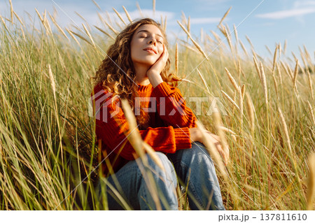 Beautiful young woman enjoying nature outdoors in tall grass. Flying hairs. Lifestyle. Fashion style Beautiful young woman enjoying nature outdoors in tall grass. Flying hairs. Lifestyle. Fashion style 137811610