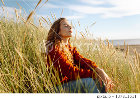 Beautiful young woman enjoying nature outdoors in tall grass. Flying hairs. Lifestyle. Fashion style Beautiful young woman enjoying nature outdoors in tall grass. Flying hairs. Lifestyle. Fashion style 137811611