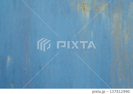 A horizontal close-up of a flat blue painted metal surface showing subtle texture, faint scratches, and small spots of orange rust. 137812990