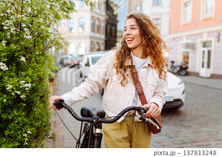 Lovely young woman posing with bike on street of city, on sunny day. Active lifestyle. Eco transport Lovely young woman posing with bike on street of city, on sunny day. Active lifestyle. Eco transport 137813248