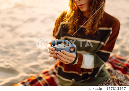 Young happy traveler tourist sits at picnic on the beach drinks hot drink. People, journey concept 137813367