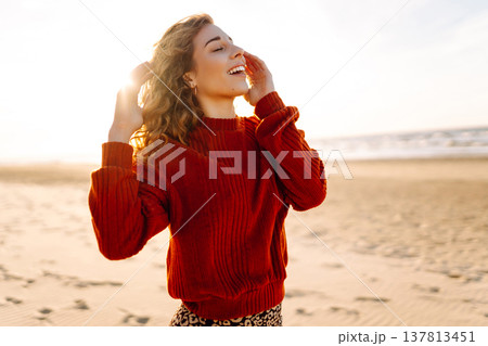 Portrait of a beautiful woman on the beach at sunset. Girl walks along the beach and enjoys weather Portrait of a beautiful woman on the beach at sunset. Girl walks along the beach and enjoys weather 137813451