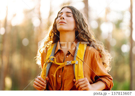 Tourist woman hiking alone in thick autumn forest. Stylish female looks for pathway among trees. Tourist woman hiking alone in thick autumn forest. Stylish female looks for pathway among trees. 137813607