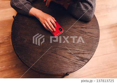 木製テーブル上の赤いスマートフォンと女性の手 木製テーブル上の赤いスマートフォンと女性の手 137813725